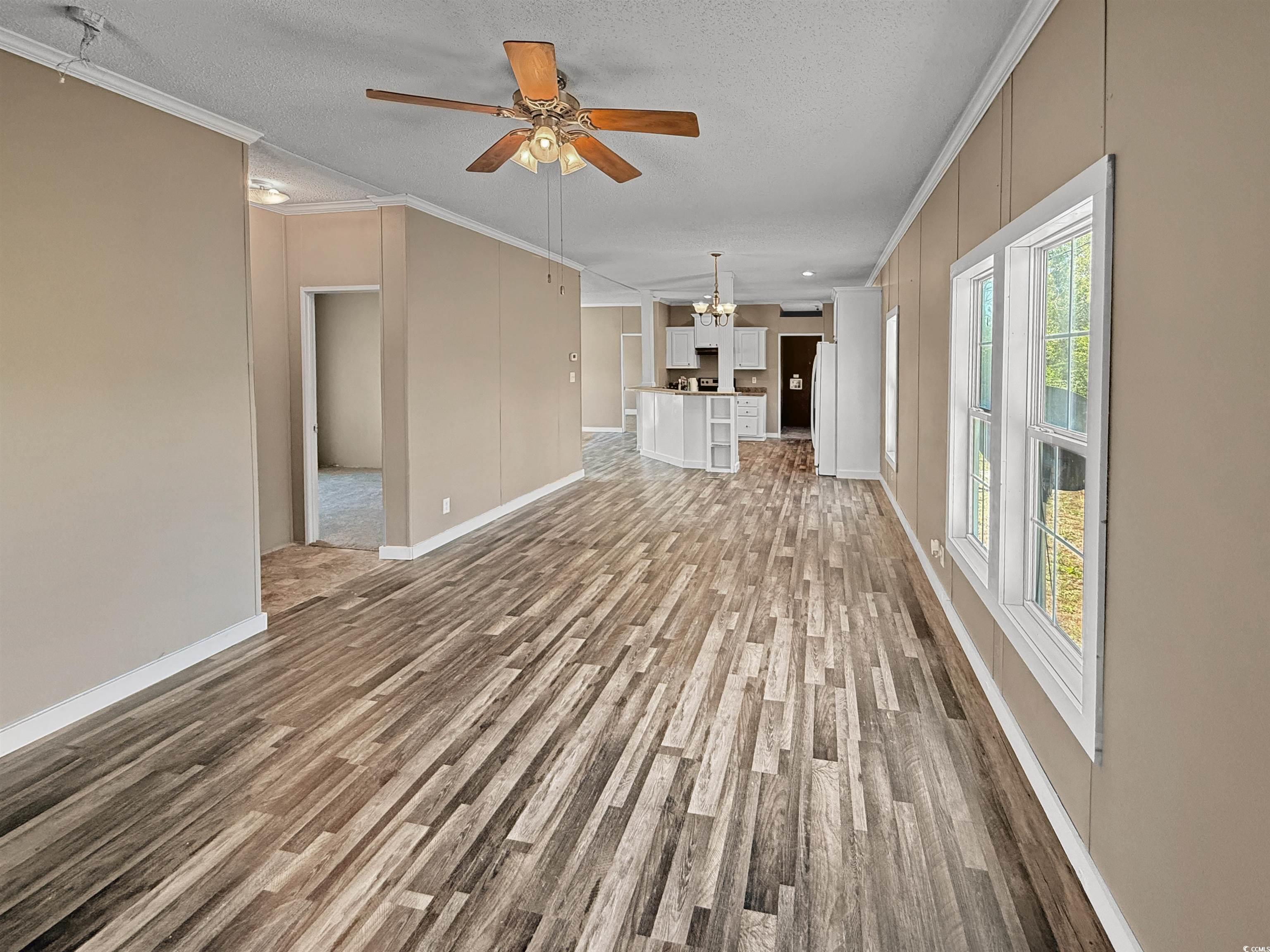 111 Morrisville Road Andrews, SC 29510 - Photo 9 of 28 Unfurnished living room with baseboards, light wood-type flooring, a textured ceiling, crown molding, and ceiling fan with notable chandelier