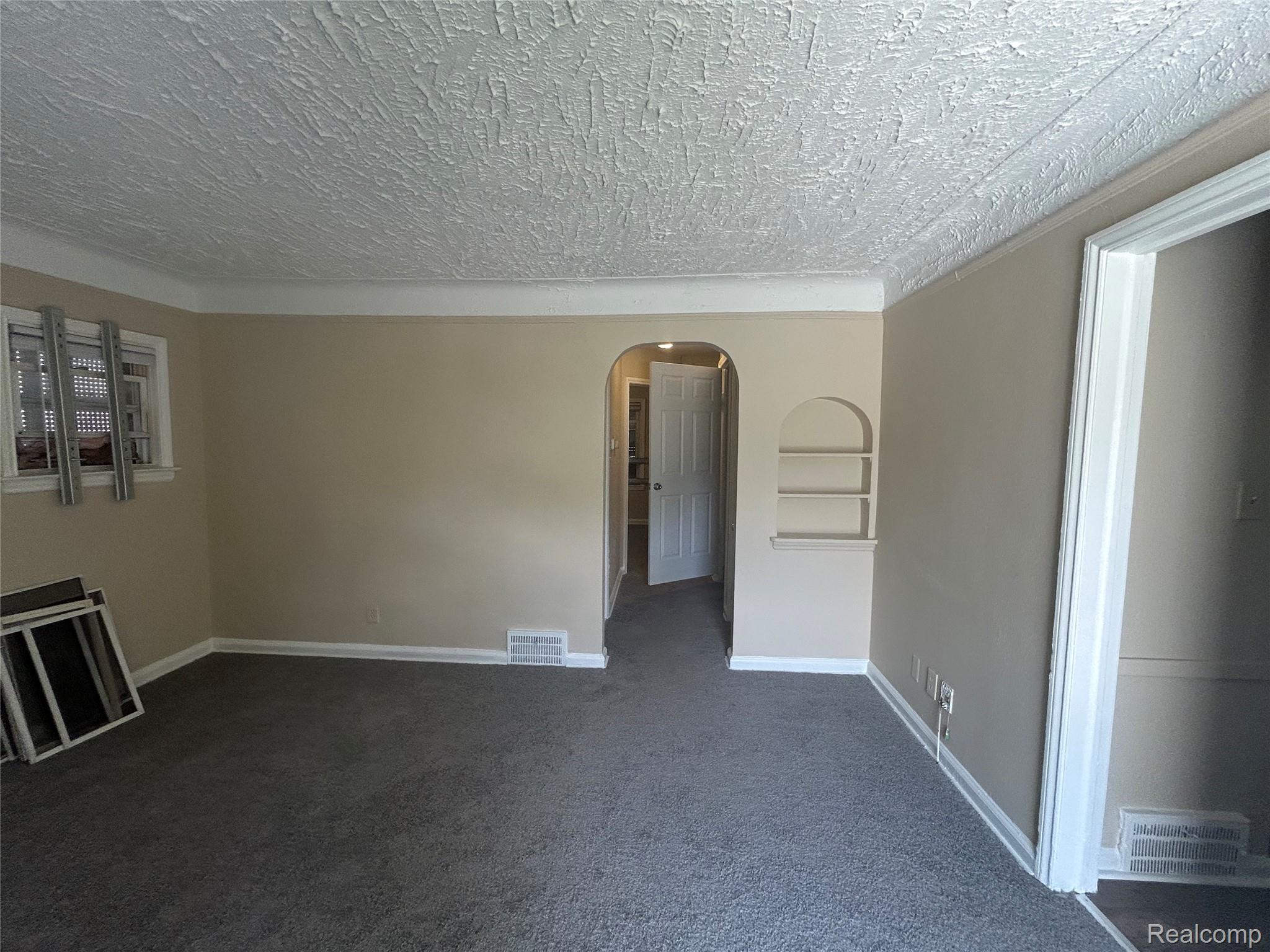 16824 Rutherford Street Detroit, MI 48235 - Photo 9 of 25 Spacious room featuring neutral tone walls, dark grey carpeting, a textured ceiling, a built-in arched display niche, and white trim