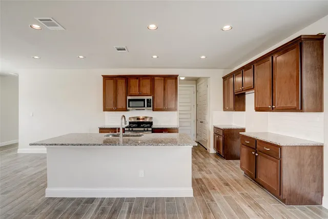 a large kitchen with stainless steel appliances granite countertop a stove a sink dishwasher a microwave oven and a dining table with wooden floor