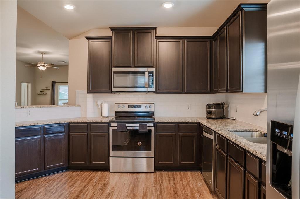 1837 Rialto Lane Crowley, TX 76036 - Photo 4 of 24 Kitchen featuring dark wood cabinetry, light-toned countertops, a white subway tile backsplash, stainless steel appliances, and wood-finish flooring