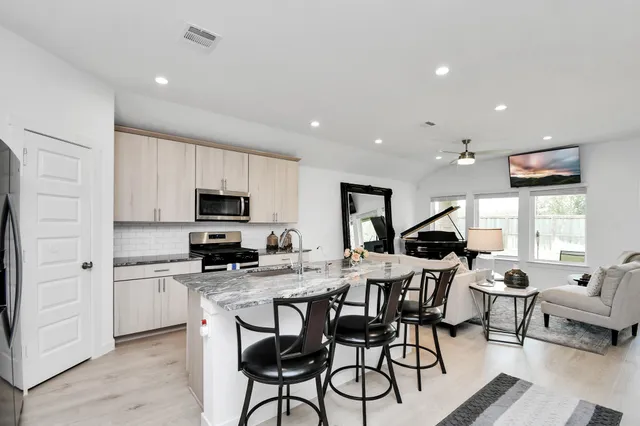 a kitchen with stainless steel appliances kitchen island granite countertop a stove a sink a refrigerator cabinets and a dining table with wooden floor