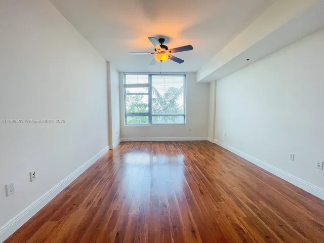 an empty room with wooden floor windows and fan
