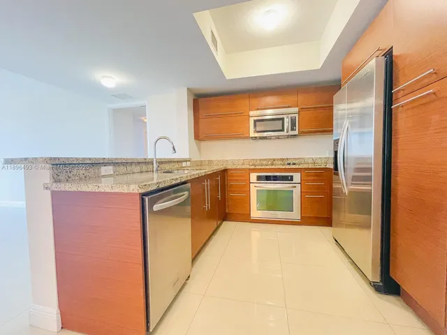 a kitchen with stainless steel appliances granite countertop a stove a sink and a refrigerator with wooden cabinets