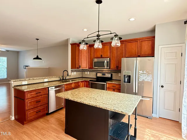 a kitchen with stainless steel appliances granite countertop a sink a stove a refrigerator a center island with wooden floor and cabinets