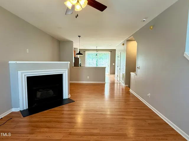 a view of an empty room with wooden floor fireplace and a window
