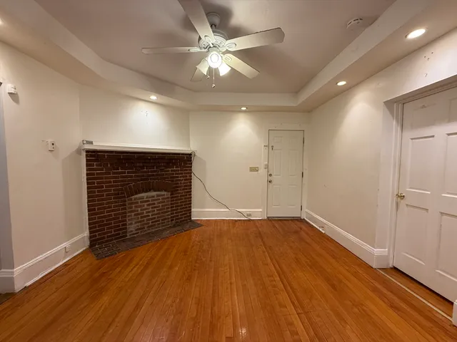 a view of an empty room with wooden floor and a ceiling fan