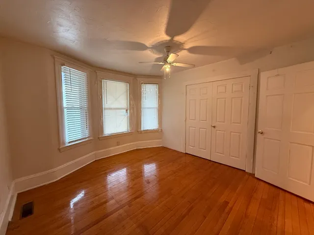 an empty room with wooden floor fan and windows