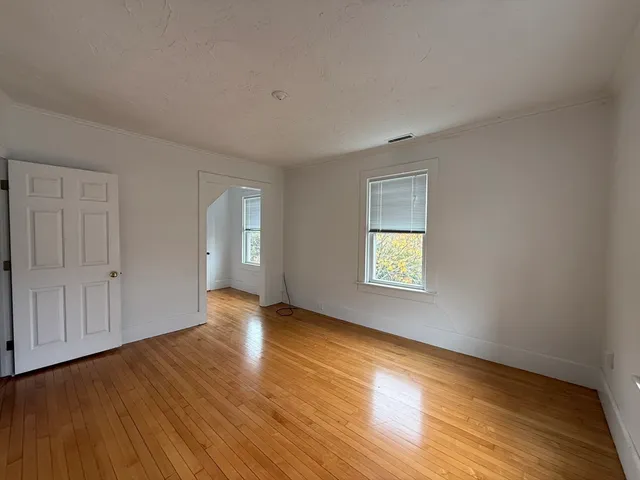 a view of an empty room with wooden floor and window