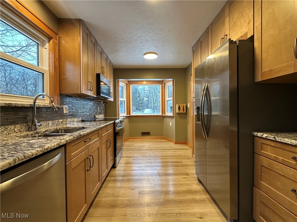 4811 West Pleasant Valley Road Cleveland, OH 44129 - Photo 6 of 31 Kitchen with light stone countertops, stainless steel appliances, brown cabinets, light wood-type flooring, and a textured ceiling