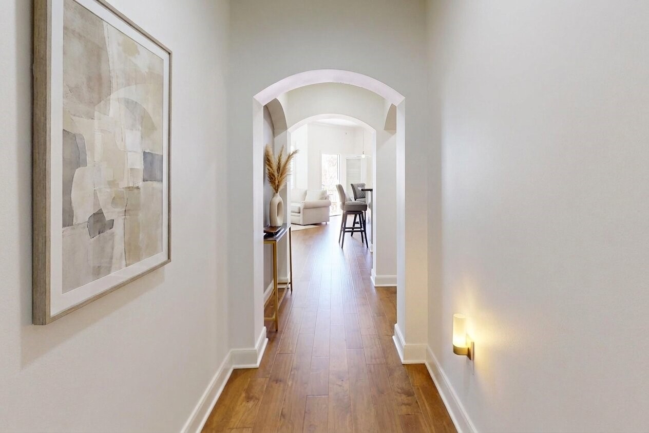 1010 Rosine Street, Unit 29 Houston, TX 77019 - Photo 13 of 16 This photo shows a bright, welcoming hallway with wooden flooring, leading to an open living area. The space is accented by modern artwork and subtle lighting, creating an inviting atmosphere. (Virtual Staging)