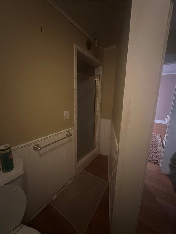 504 1st Street Terrell, TX 75160 - Photo 18 of 27 Full bathroom featuring a shower stall with clear glass enclosure and tile surround, wood-finish flooring, white beadboard wainscoting, and a wall-mounted light fixture