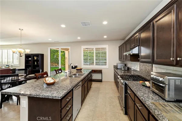 a kitchen with stainless steel appliances granite countertop a stove top oven a sink dishwasher a dining table and chairs with wooden floor