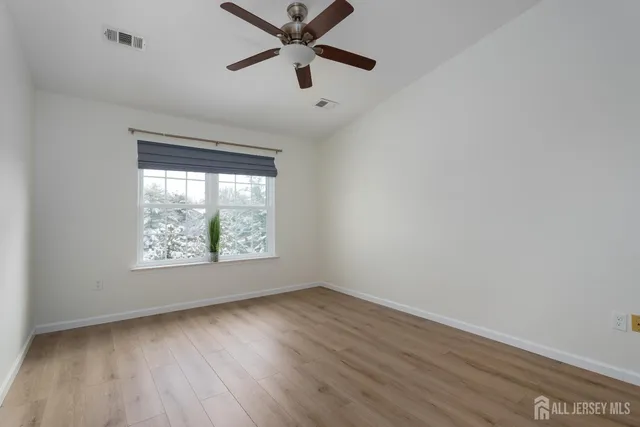 an empty room with wooden floor fan and windows