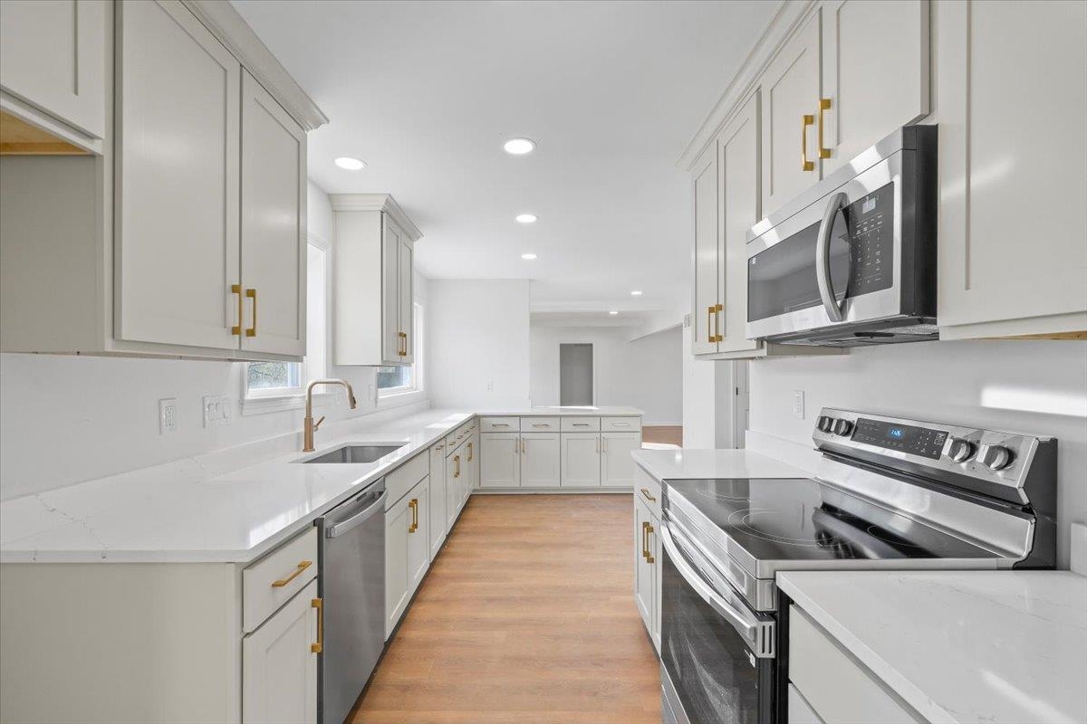 1676 Miller Farms Road Germantown, TN 38138 - Photo 14 of 37 Modern kitchen featuring white shaker cabinetry, gold-tone hardware, stainless steel appliances, white countertops, and wood-finish flooring