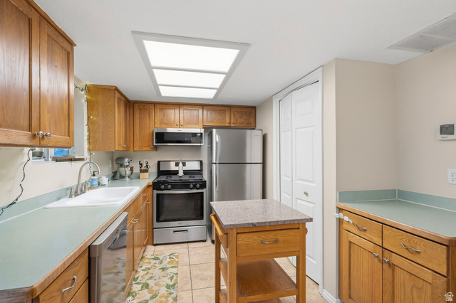1099 South 950 East, Unit 17 Provo, UT 84606 - Photo 8 of 23 Kitchen featuring wood cabinetry, light-toned countertops, tile flooring, stainless steel appliances, and a central island with a granite-look top