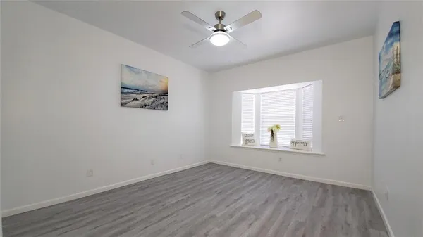 an empty room with wooden floor chandelier fan and windows