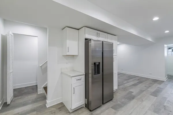 a view of a refrigerator in kitchen and an empty room with wooden floor