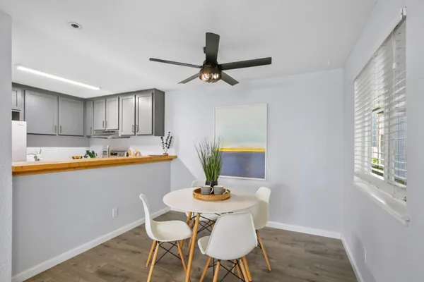 a white kitchen with stainless steel appliances granite countertop a sink a stove a dining table and chairs with wooden floor