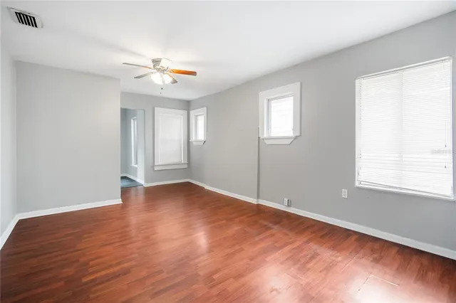 an empty room with wooden floor chandelier fan and windows