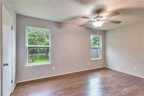 an empty room with wooden floor windows and fan