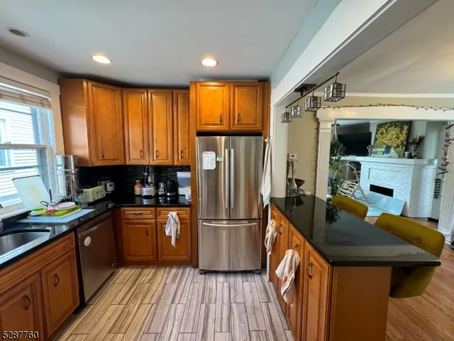 a kitchen with stainless steel appliances granite countertop a refrigerator a sink dishwasher a stove and a dining table with wooden floor