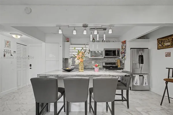 a kitchen with stainless steel appliances kitchen island granite countertop a dining table chairs and a refrigerator