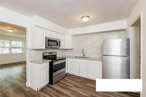 a kitchen with stainless steel appliances a refrigerator a stove top oven a sink and white cabinets