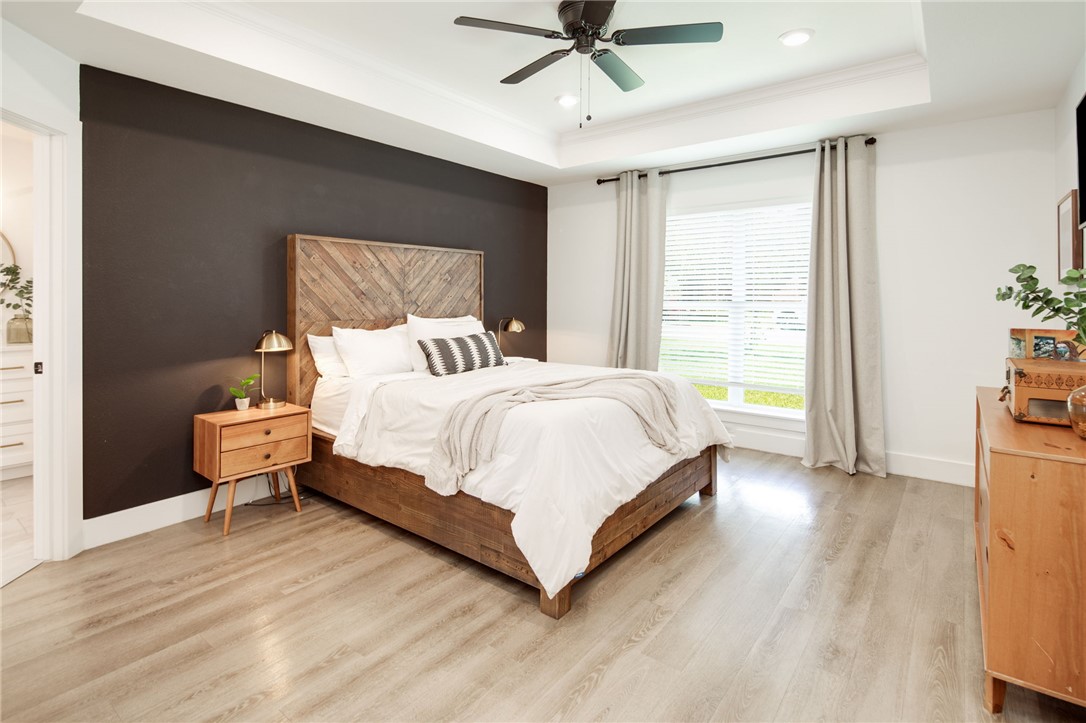 4700 Kensington Road Bryan, TX 77802 - Photo 14 of 31 Spacious primary bedroom featuring wood-finish flooring, a tray ceiling with a ceiling fan, recessed lighting, and a large window with blinds and drapes