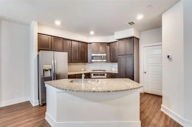 a kitchen with stainless steel appliances granite countertop a refrigerator a stove and a sink with wooden floor