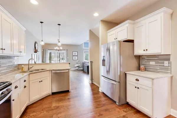 a kitchen with stainless steel appliances granite countertop a refrigerator a sink dishwasher a stove and white cabinets with wooden floor