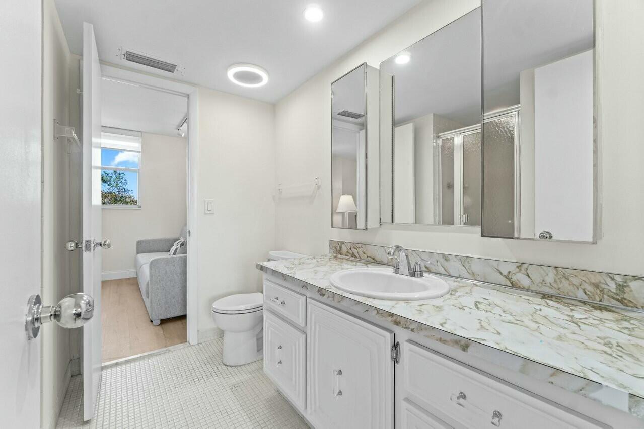 6461 Northwest 2nd Avenue, Unit 411 Boca Raton, FL 33487 - Photo 22 of 34 a bathroom with a granite countertop sink a toilet and a mirror