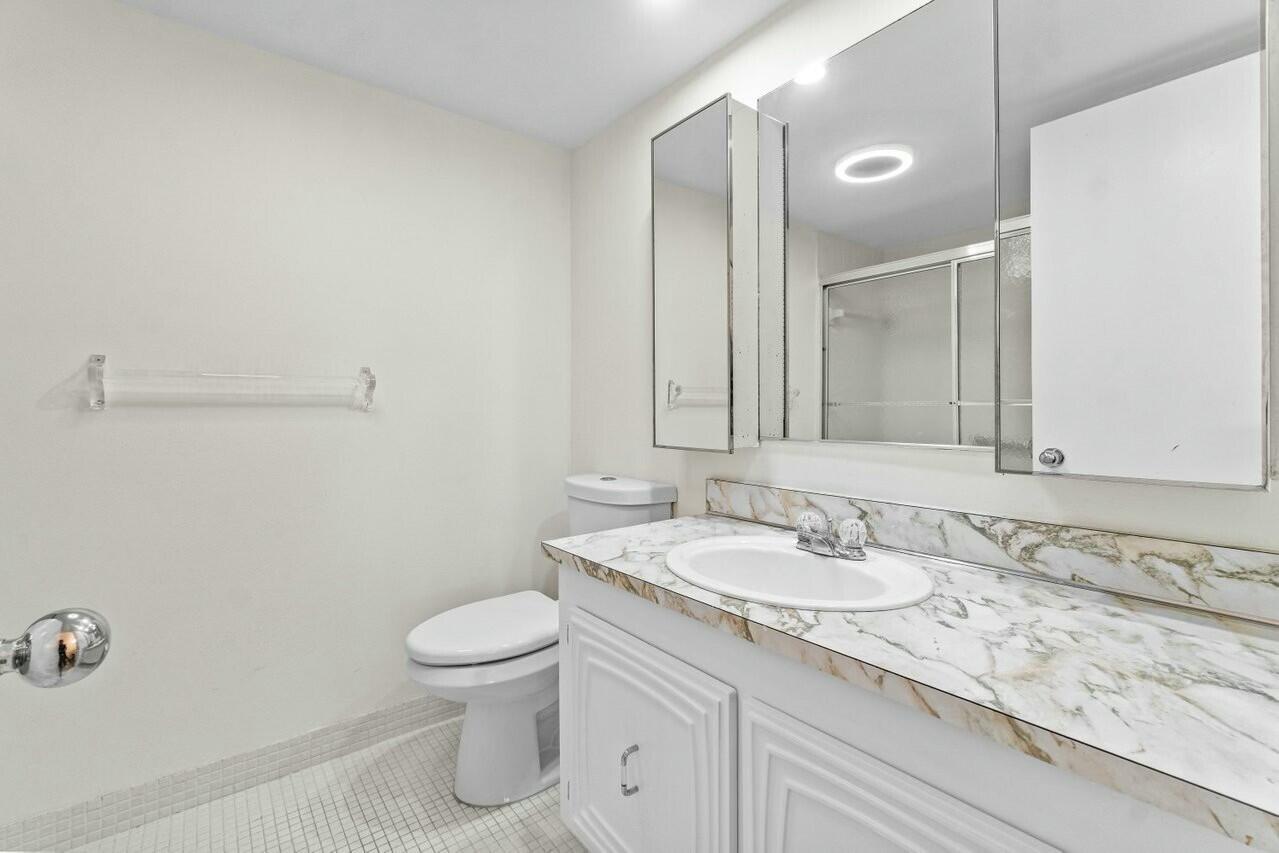 6461 Northwest 2nd Avenue, Unit 411 Boca Raton, FL 33487 - Photo 23 of 34 a bathroom with a granite countertop sink a toilet and a mirror
