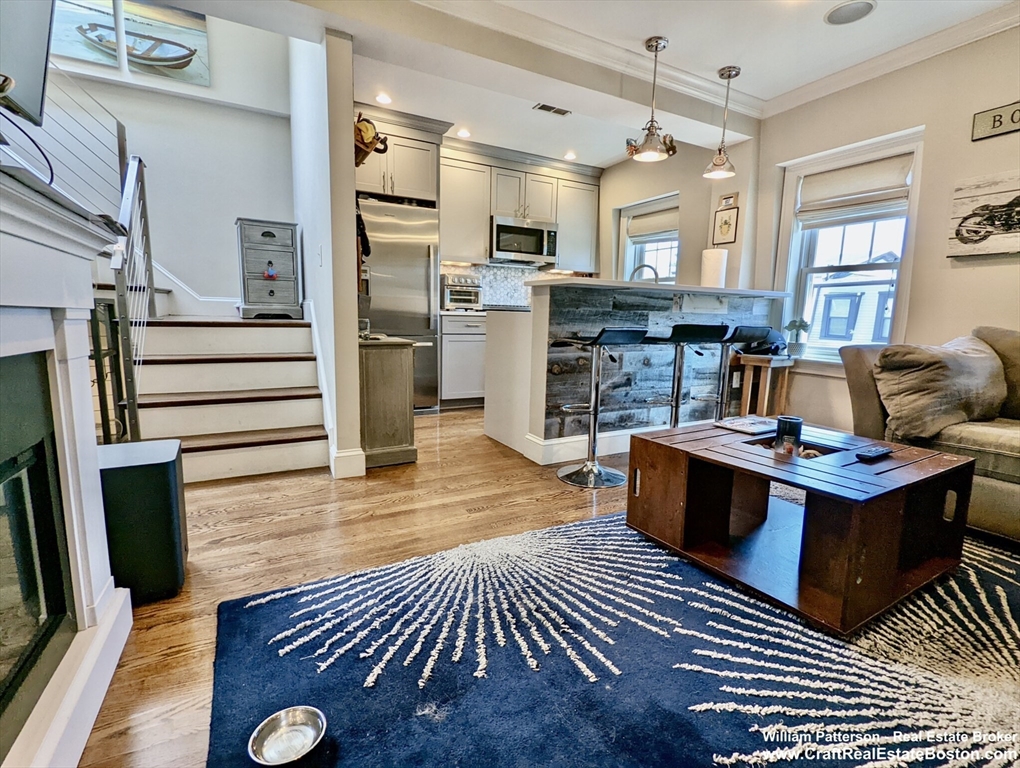 a living room with stainless steel appliances furniture a rug kitchen view and a window