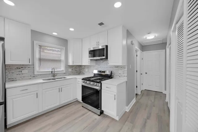 a kitchen with stainless steel appliances granite countertop a stove top oven a sink and white cabinets