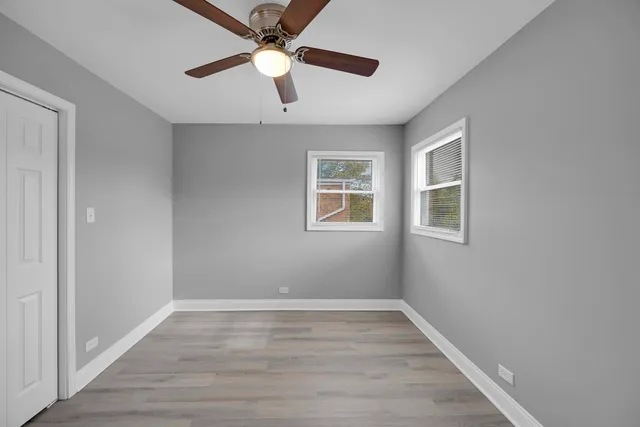 an empty room with wooden floor ceiling fan and windows