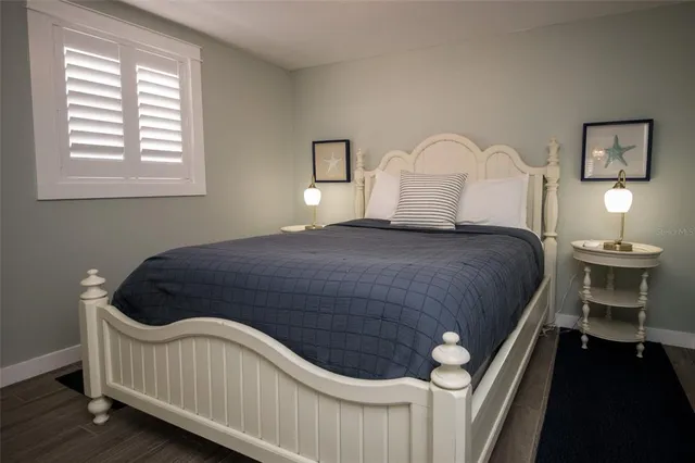a bed sitting in a bedroom and a lamp on dresser with wooden floor