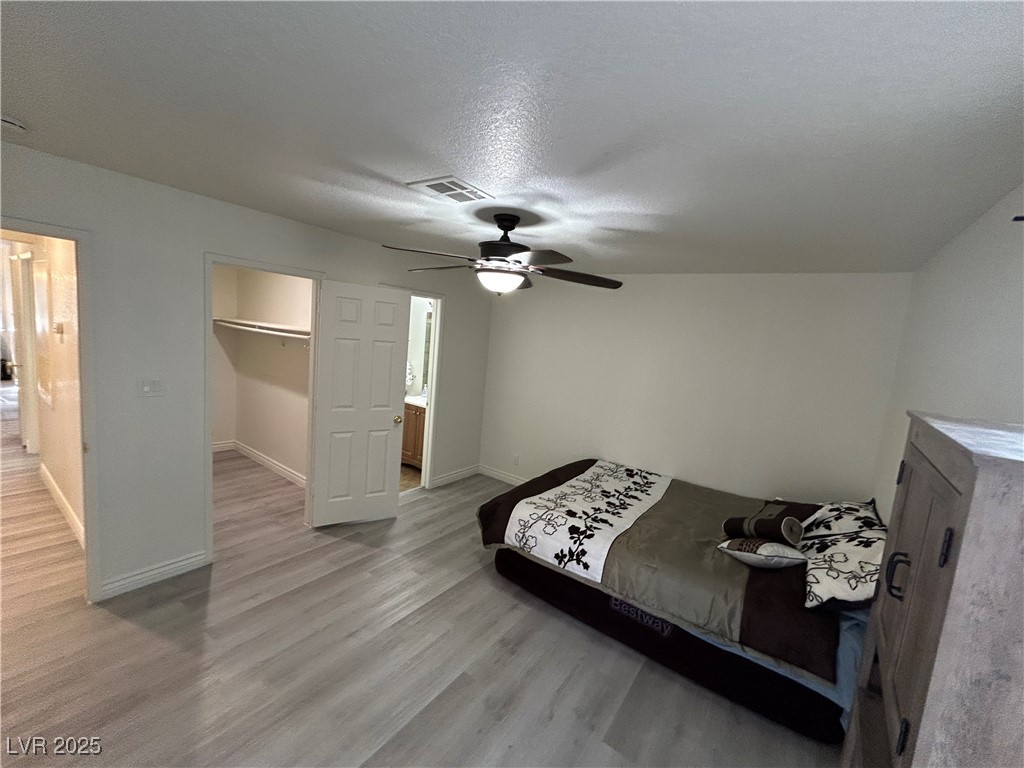 5044 South Rainbow Boulevard, Unit 106 Las Vegas, NV 89118 - Photo 11 of 18 Bedroom with light wood-style floors, a ceiling fan, a walk in closet, and a textured ceiling