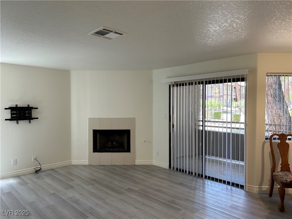 5044 South Rainbow Boulevard, Unit 106 Las Vegas, NV 89118 - Photo 3 of 18 Unfurnished living room featuring wood finished floors, a textured ceiling, healthy amount of natural light, and a tiled fireplace