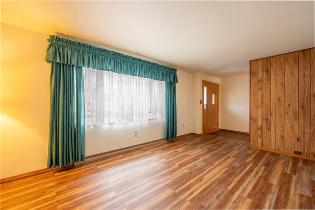 an empty room with wooden floor and windows with curtains