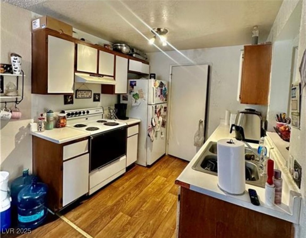 221 Mission Newport Lane, Unit 205 Las Vegas, NV 89107 - Photo 10 of 11 Kitchen featuring white appliances, light wood-style flooring, light countertops, under cabinet range hood, and a textured ceiling