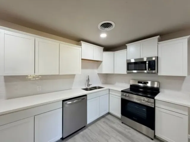 a kitchen with granite countertop white cabinets stainless steel appliances and a sink