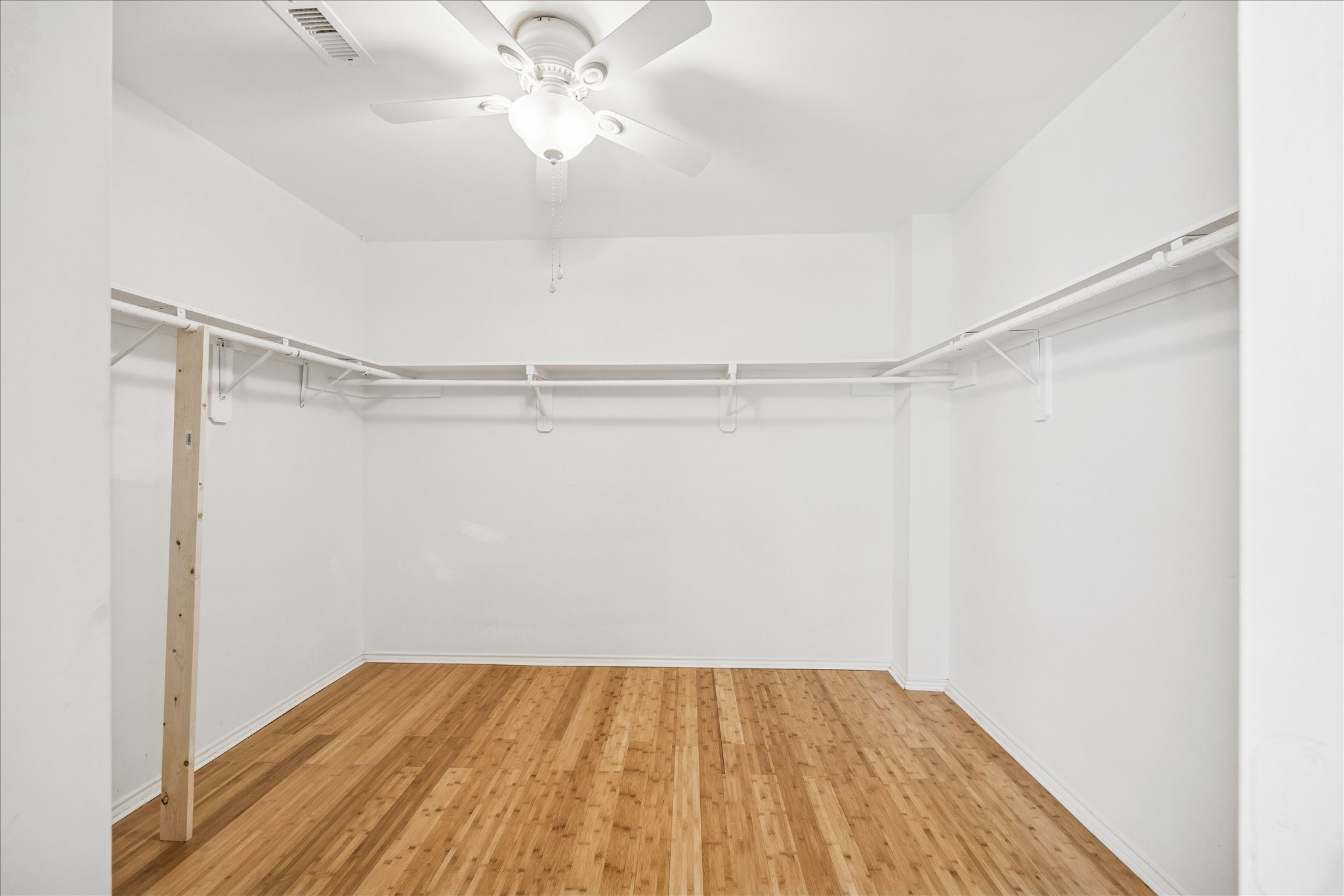 2607 Link Road Houston, TX 77009 - Photo 19 of 21 Spacious walk-in, Primary closet with wooden flooring, white walls, and ample hanging space. A ceiling fan provides ventilation and light.