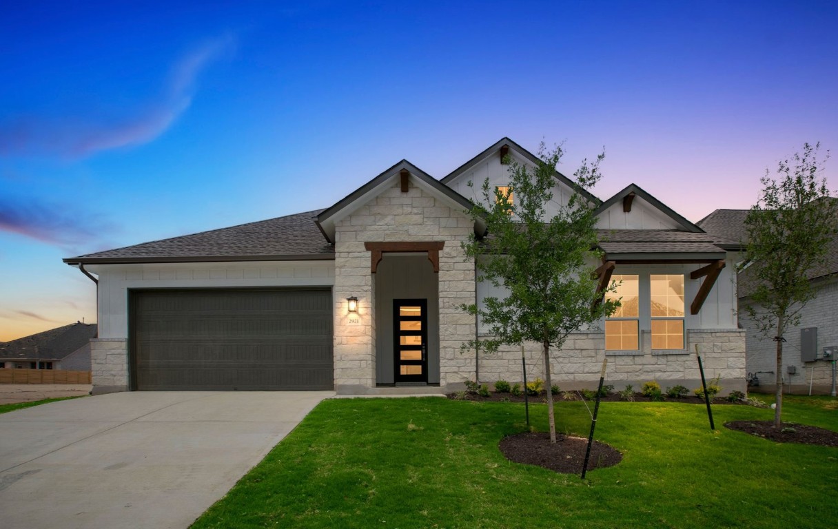 View of front facade featuring an attached garage, stone siding, and concrete driveway