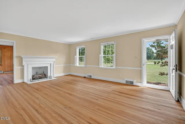 an empty room with wooden floor fireplace and windows