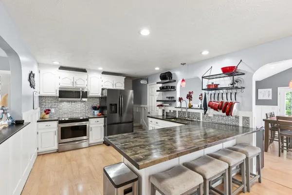 a kitchen with stainless steel appliances granite countertop a stove top oven a sink a dining table and chairs