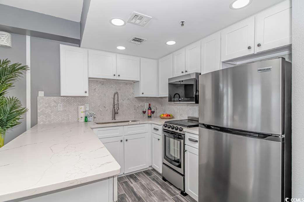 1605 South Ocean Boulevard, Unit 603 Myrtle Beach, SC 29577 - Photo 14 of 40 Kitchen featuring appliances with stainless steel finishes, white cabinetry, tasteful backsplash, a peninsula, and recessed lighting