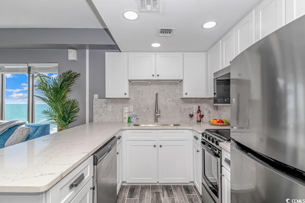 1605 South Ocean Boulevard, Unit 603 Myrtle Beach, SC 29577 - Photo 15 of 40 Kitchen featuring appliances with stainless steel finishes, white cabinets, light stone countertops, and recessed lighting