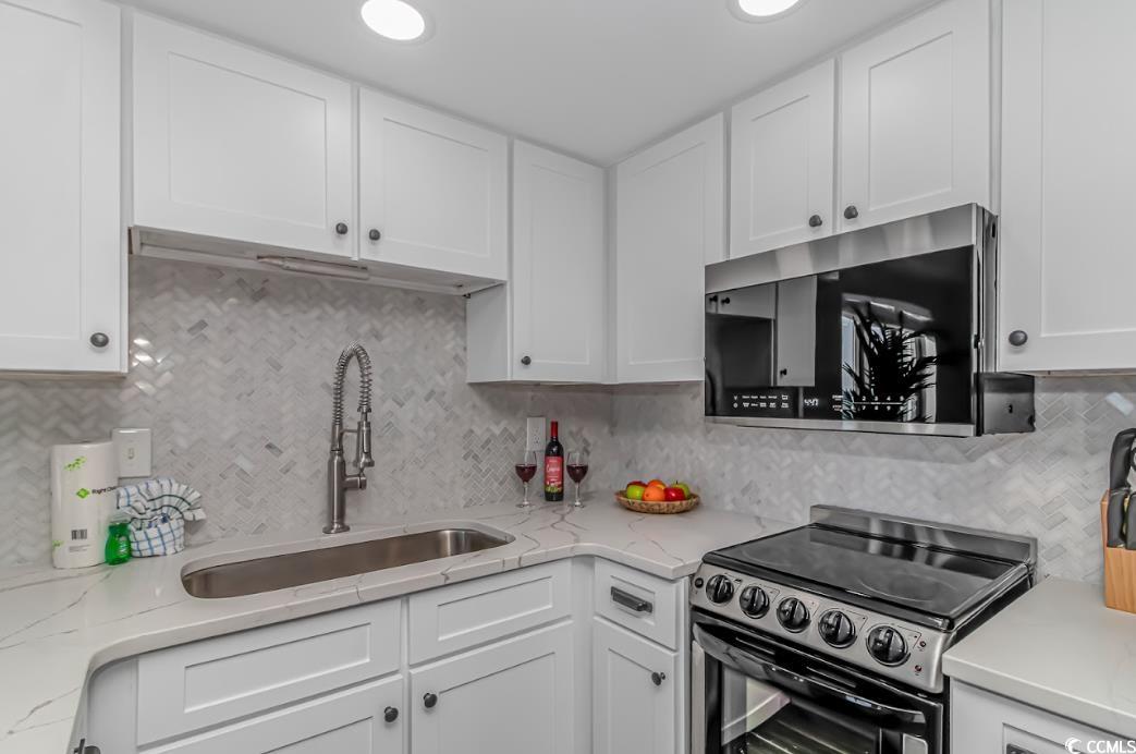 1605 South Ocean Boulevard, Unit 603 Myrtle Beach, SC 29577 - Photo 16 of 40 Kitchen with electric stove, tasteful backsplash, white cabinets, stainless steel microwave, and light stone countertops