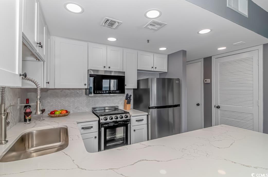 1605 South Ocean Boulevard, Unit 603 Myrtle Beach, SC 29577 - Photo 18 of 40 Kitchen featuring stainless steel appliances, white cabinets, light stone countertops, backsplash, and recessed lighting