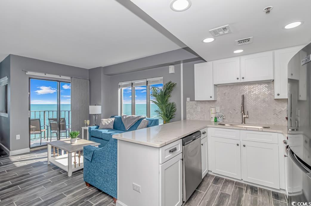1605 South Ocean Boulevard, Unit 603 Myrtle Beach, SC 29577 - Photo 38 of 40 Kitchen with decorative backsplash, wood finish floors, white cabinets, open floor plan, and light stone counters